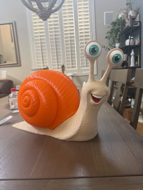A smiling 3D printed snail with a bright orange shell